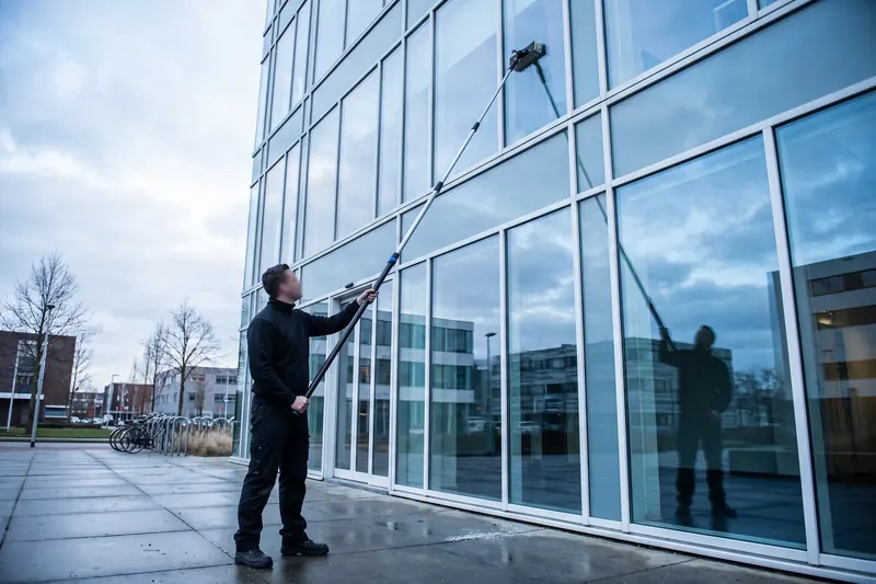 Glazenwasser reinigt vanaf de begane grond een kantoorgevel met een telescopische zuiverwaterstok